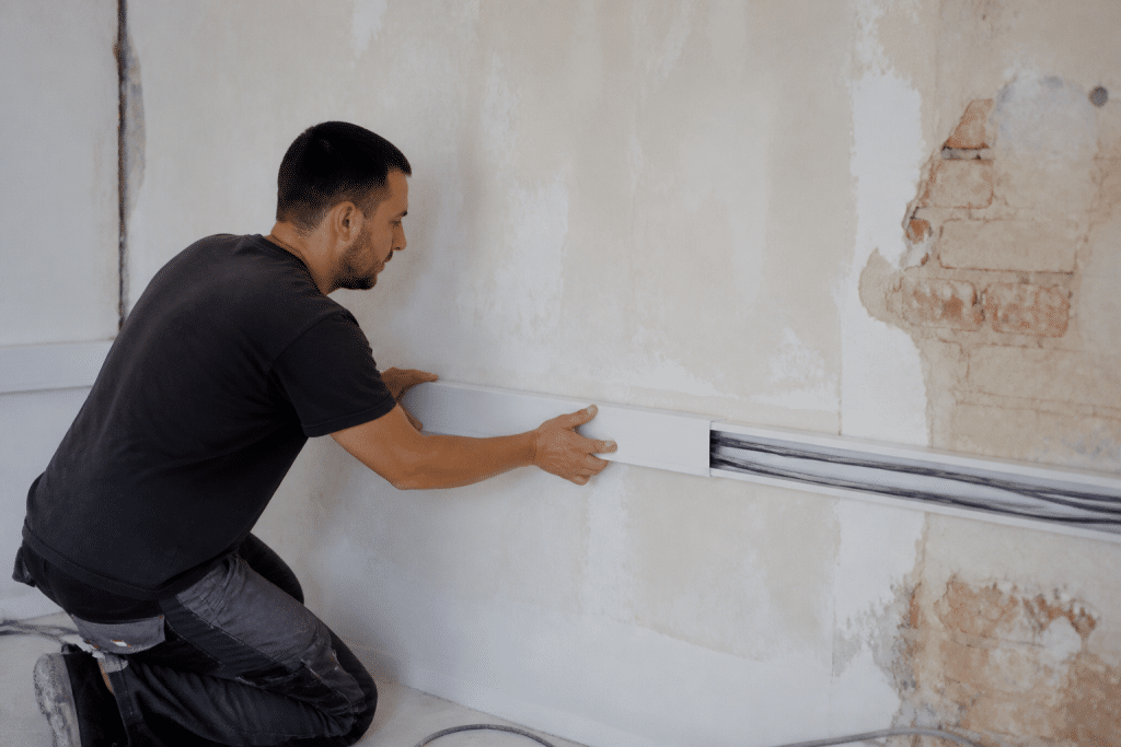 Electricien installant goulotte blanche sur mur de renovation