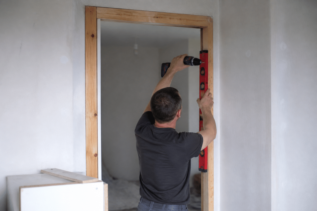 Bricoleur installant cadre porte avec niveau et perceuse
