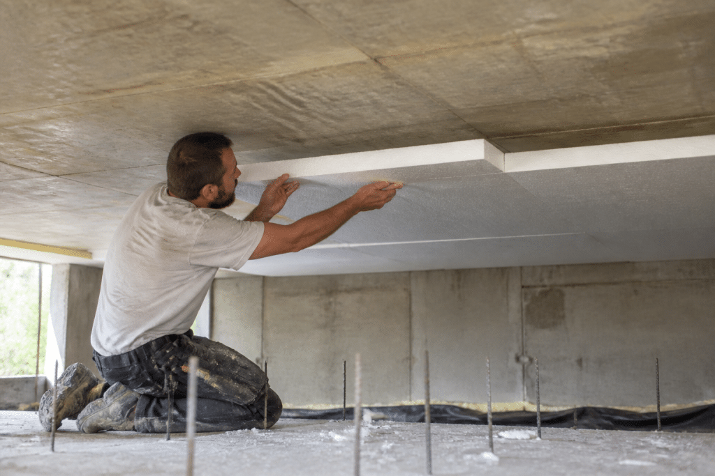 Ouvrier posant isolant mousse sous plancher beton chantier
