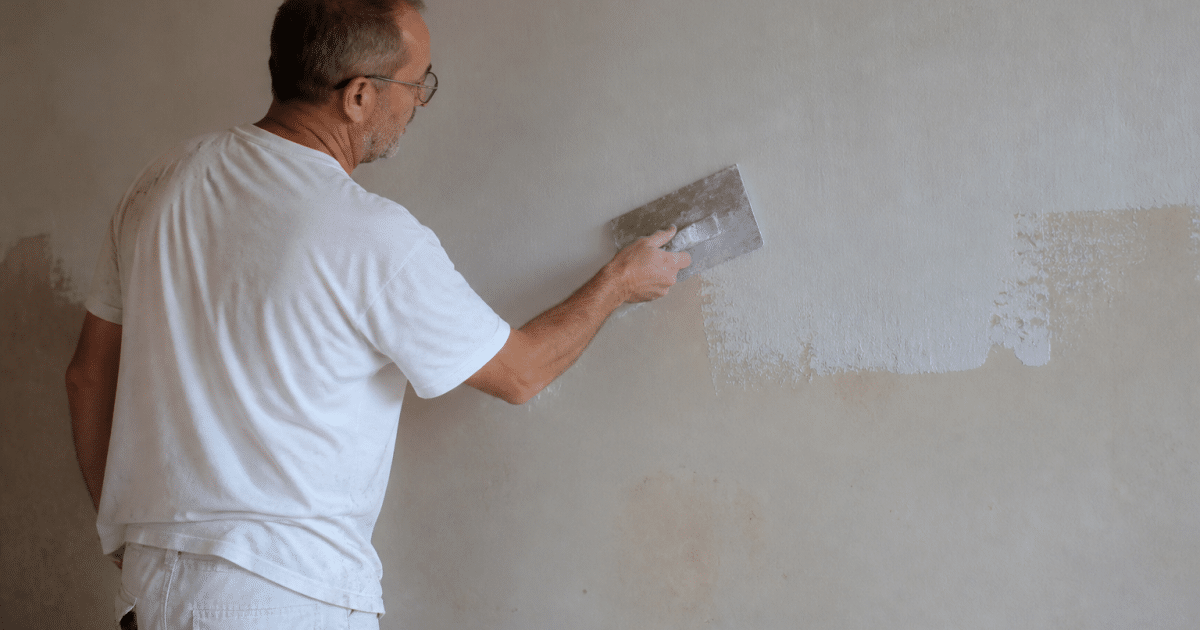 Ouvrier appliquant enduit blanc sur mur intérieur horizontal