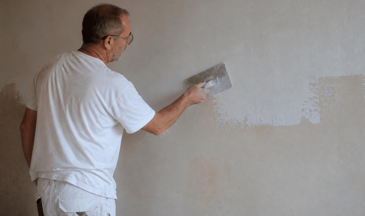 Ouvrier appliquant enduit blanc sur mur intérieur horizontal