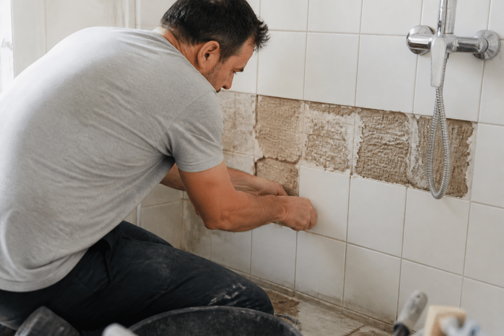Ouvrier reparant carreaux casses sur mur de salle bain